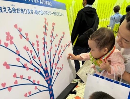 「助け合いのツリー」にシールを貼る赤ん坊